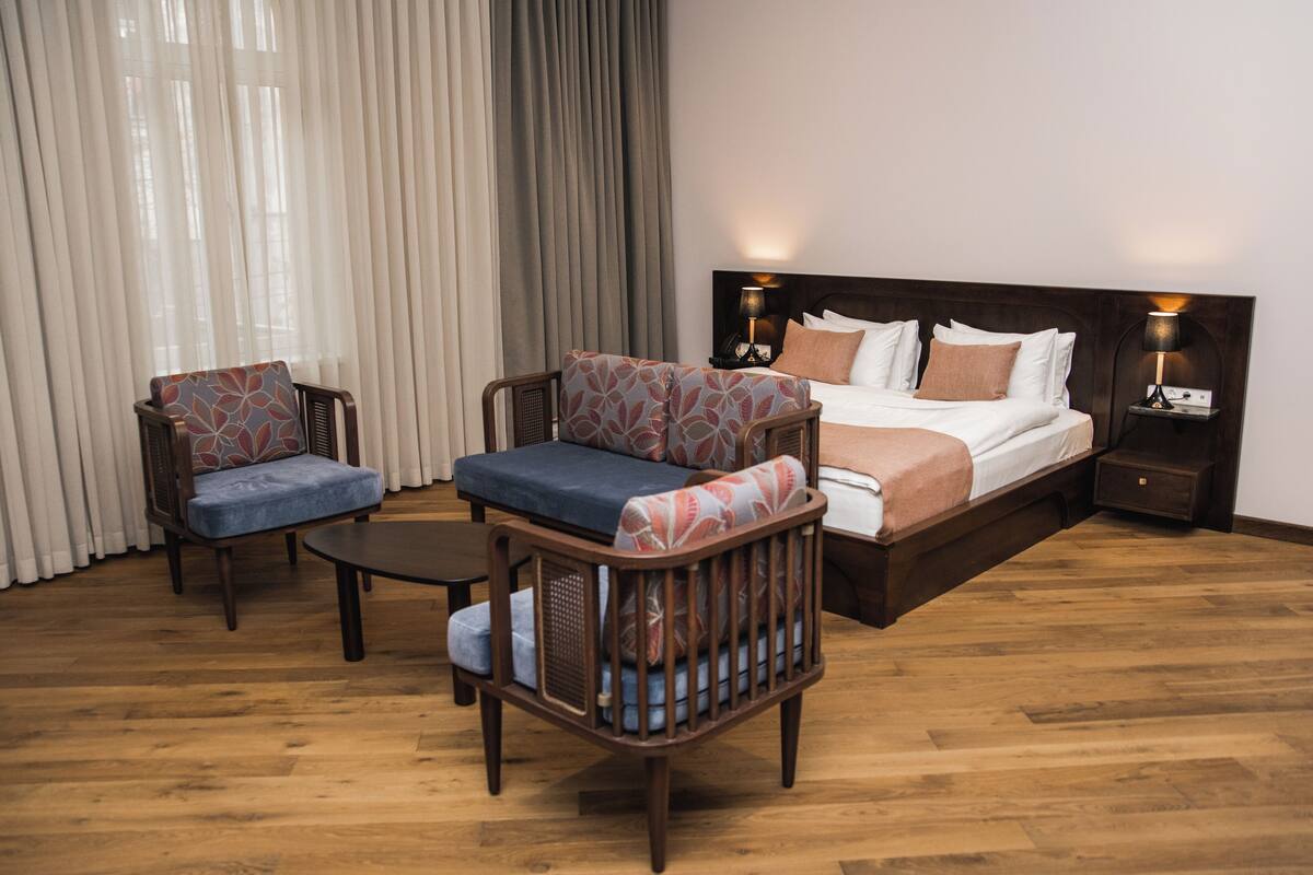 A hotel room with a large bed, two armchairs, a small table, and a nightstand with lamps.