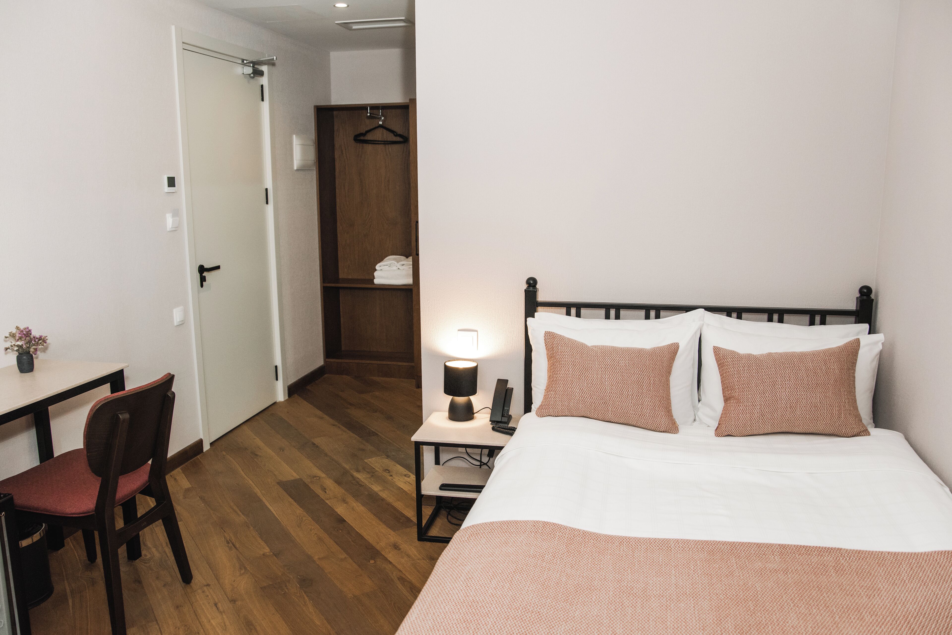 Quarto de hotel com cama, mesa de cabeceira, luminária, cadeira e armário.