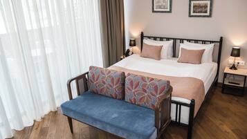 A hotel room with a bed, a bench, a nightstand, and a wall with two framed pictures.