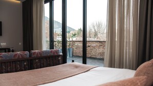 Quarto de hotel com uma cama grande, vista do exterior por uma porta de vidro e uma parede de tijolos lá fora.