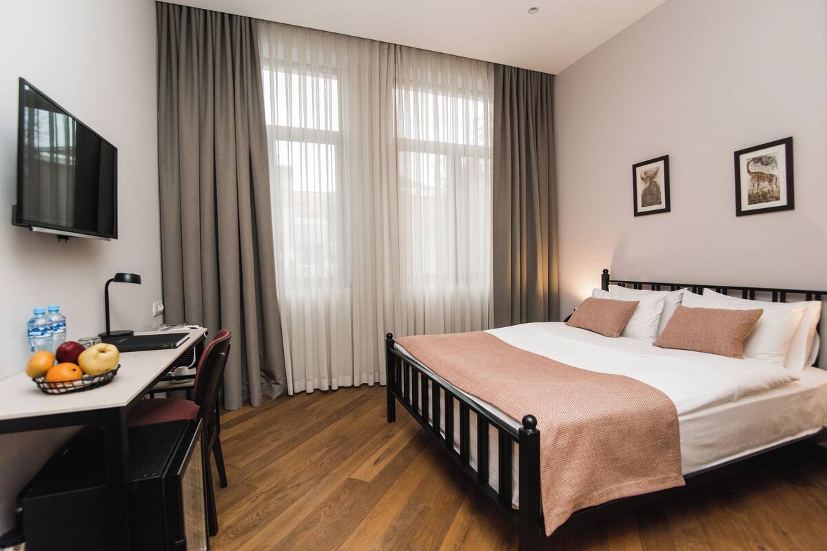 A hotel room with a bed, a desk, a chair, a TV, and curtains.
