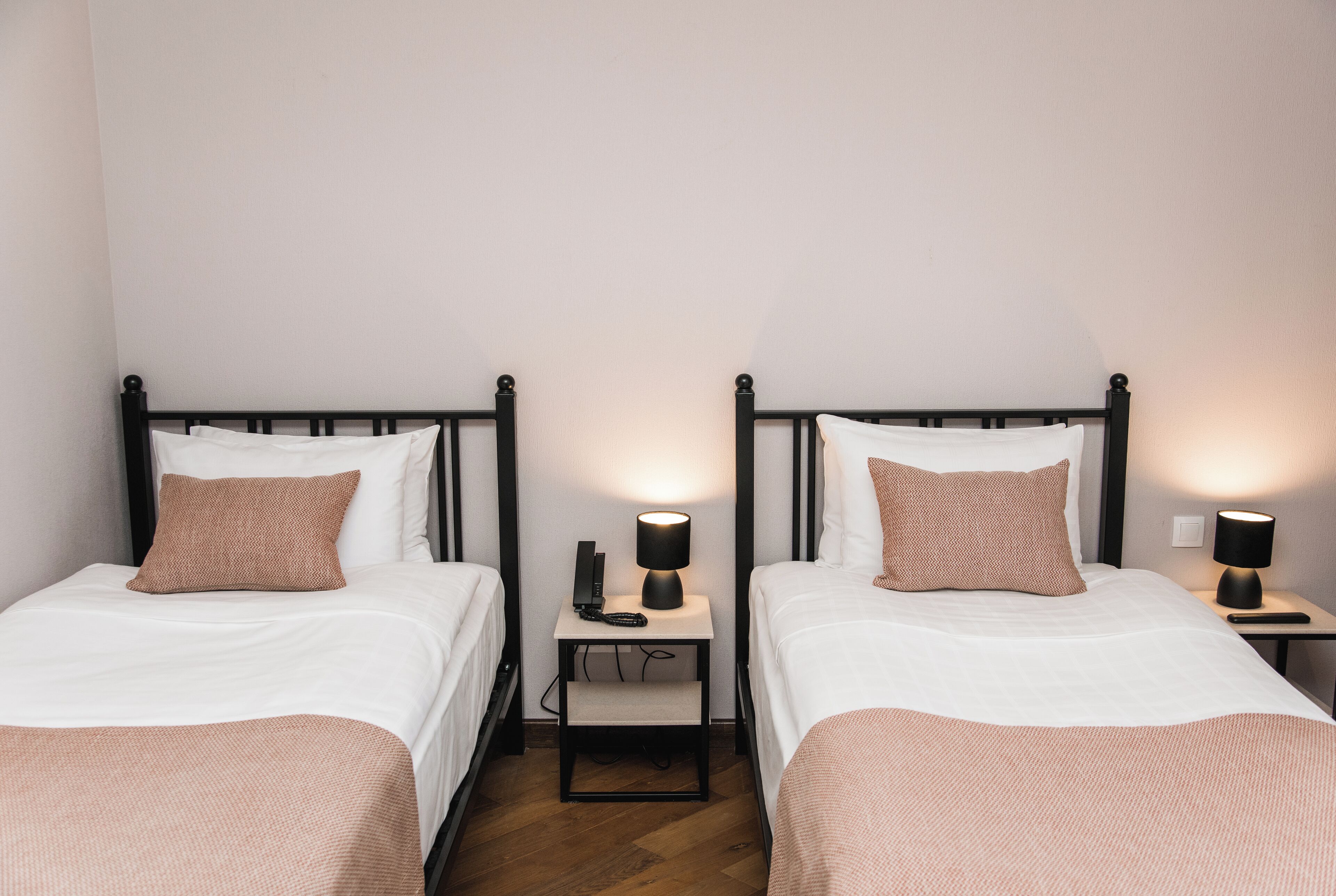Two single beds with black frames, white bedding, and brown pillows. Each bed has a bedside table with a lamp.