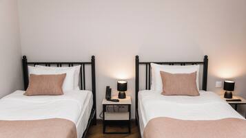 Two single beds with black frames, white bedding, and brown pillows. Each bed has a bedside table with a lamp.