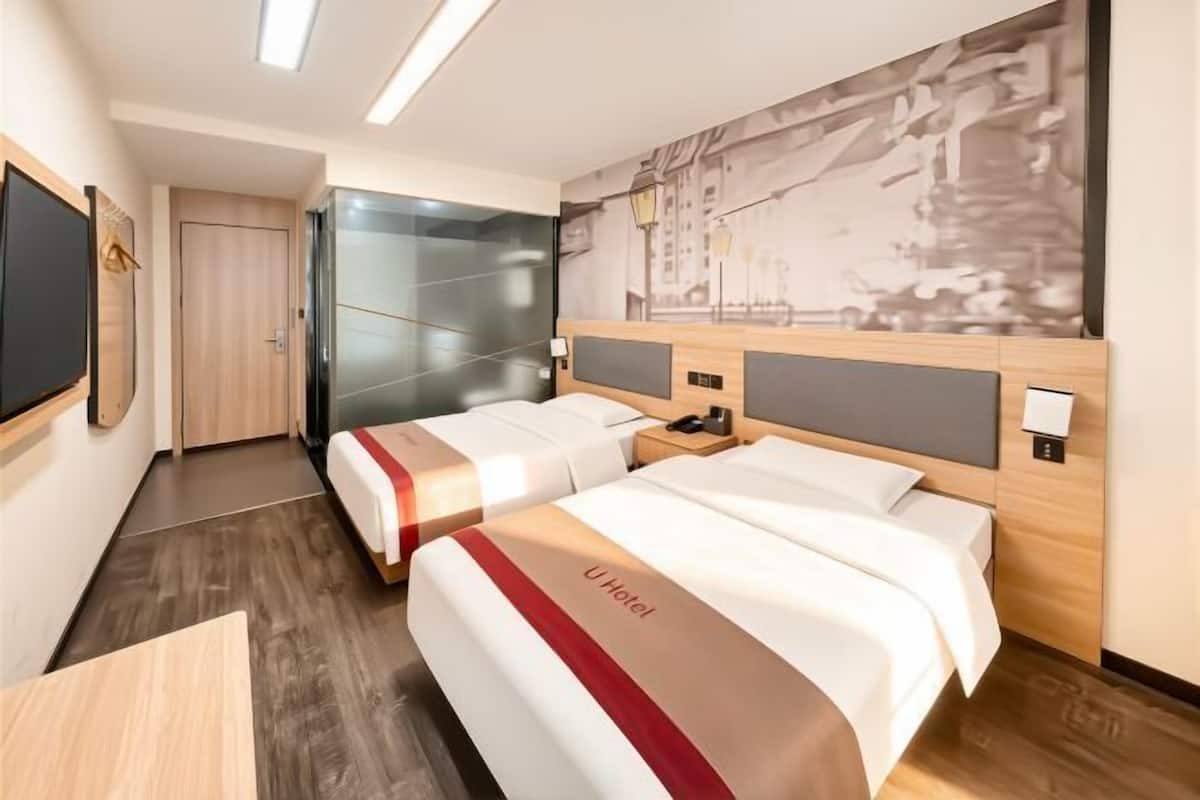 A hotel room with two beds, a wooden headboard, a flat-screen TV, and a cityscape mural on the wall.