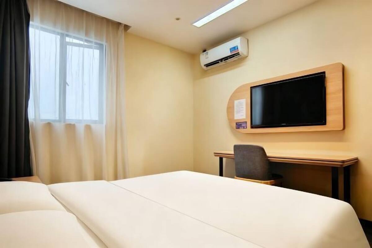 A hotel room with a bed, a desk, a chair, a television, and an air conditioning unit.