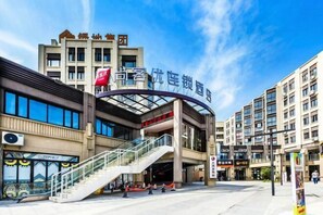 A hotel with a modern architectural design, featuring a prominent entrance with a glass facade, a staircase leading to the lobby, and a clear sky above. - Shankee Hotel (Shanghai Jinshan Wanda) (Shanghai)