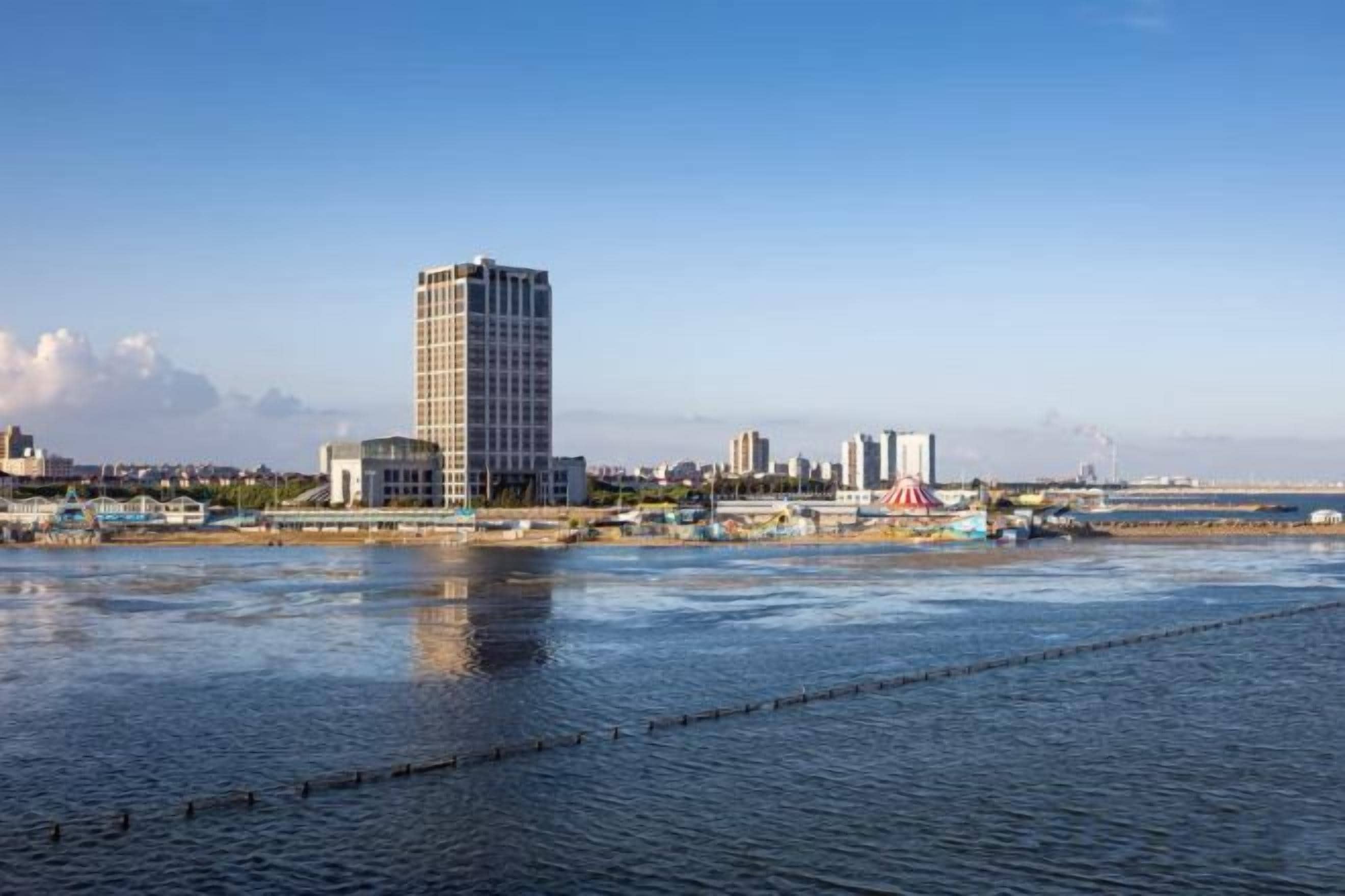 A waterfront cityscape with a prominent high-rise building, a marina, and a clear sky.