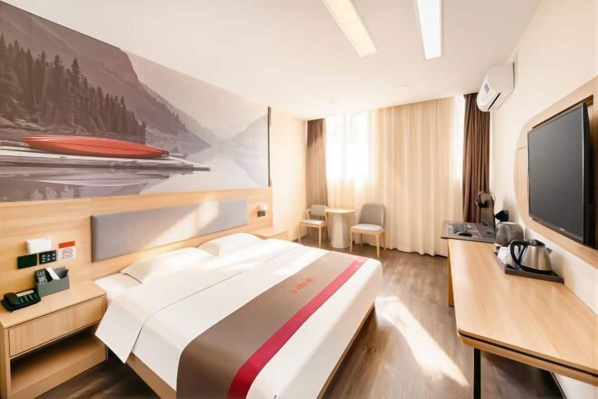 A hotel room with a bed, a desk, a chair, a television, and a painting on the wall.