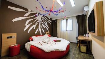 A hotel room with a red bean bag bed, a wooden headboard, a small desk, and a large window with curtains.