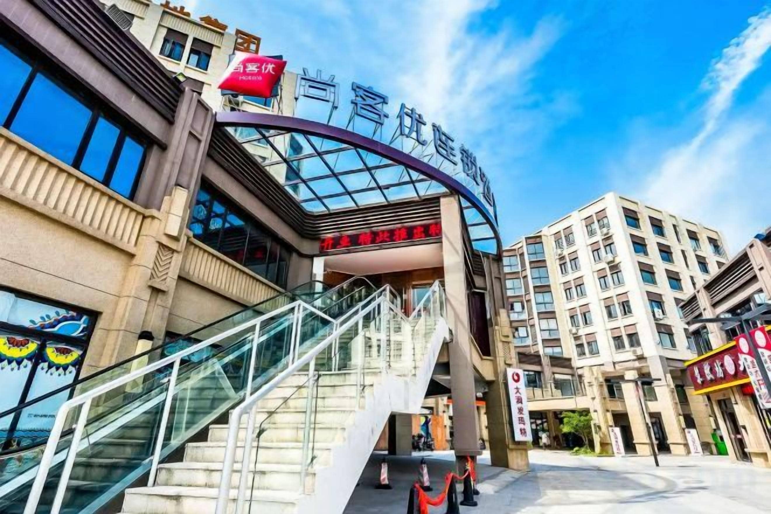 A hotel entrance with a curved glass facade, a staircase, and a clear sky.