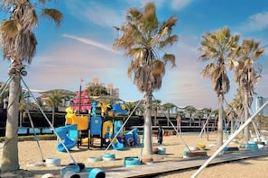 A beach playground with palm trees, a wooden boardwalk, and a cityscape in the background. - Shankee Hotel (Shanghai Jinshan Wanda) (Shanghai)