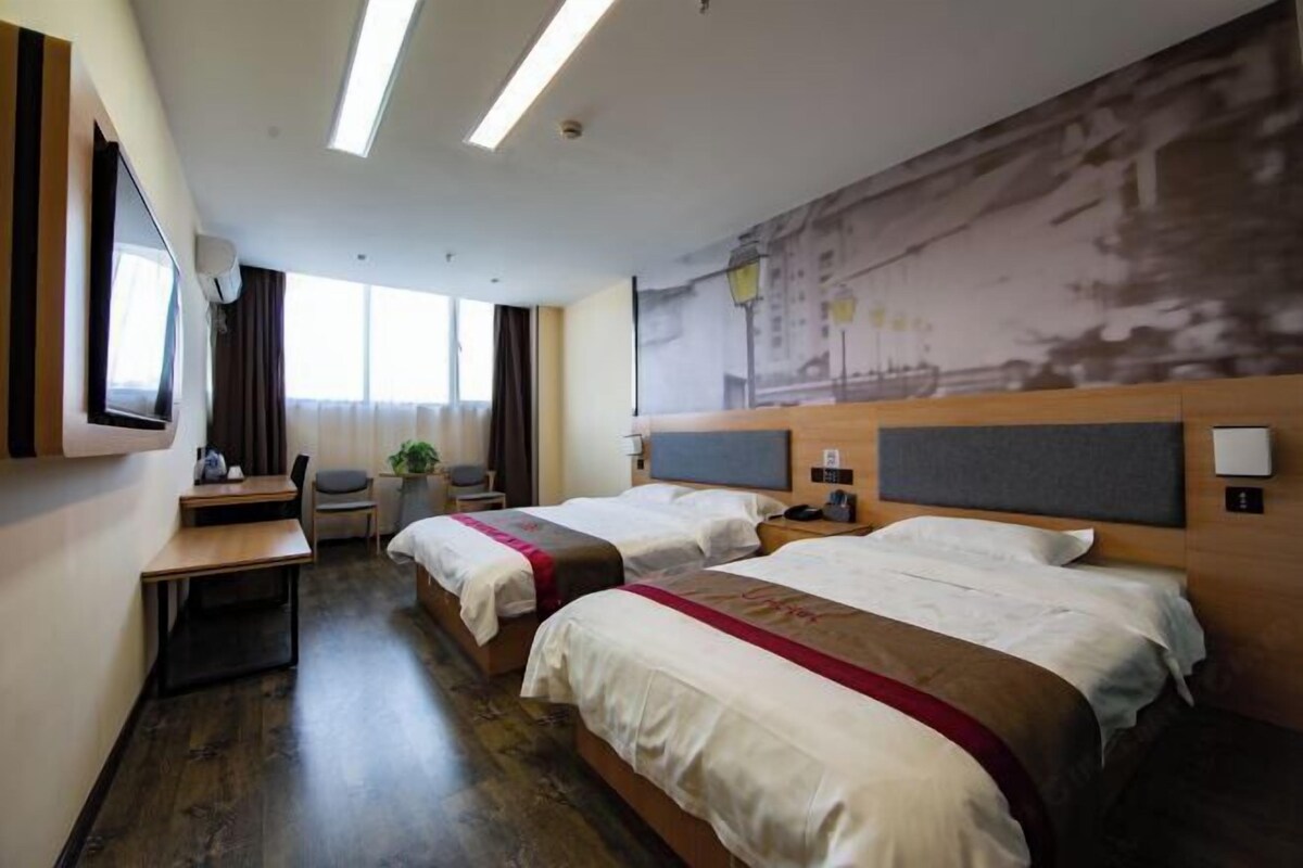 A hotel room with two beds, a desk, a chair, a TV, and a large window.