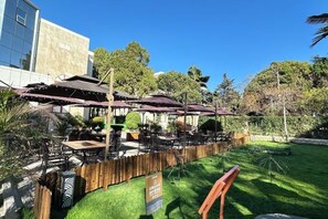 An outdoor seating area with tables and umbrellas, surrounded by a wooden fence and greenery. - Lian Yun Hotel (Kunming)