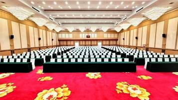 A conference room with rows of chairs, a red carpet, and a stage.