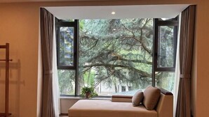 Ein Zimmer mit großem Fenster, einer Couch, einem Holzstuhl und einem Blumentopf.