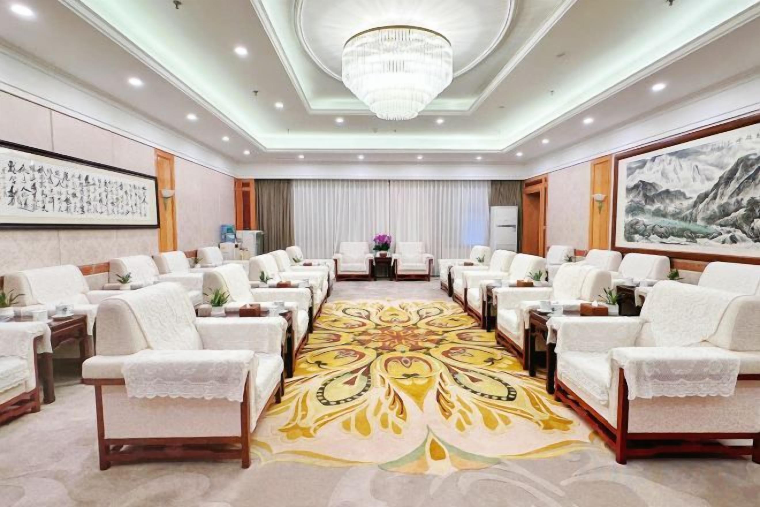 A hotel conference room with rows of white sofas, a patterned carpet, and a chandelier.