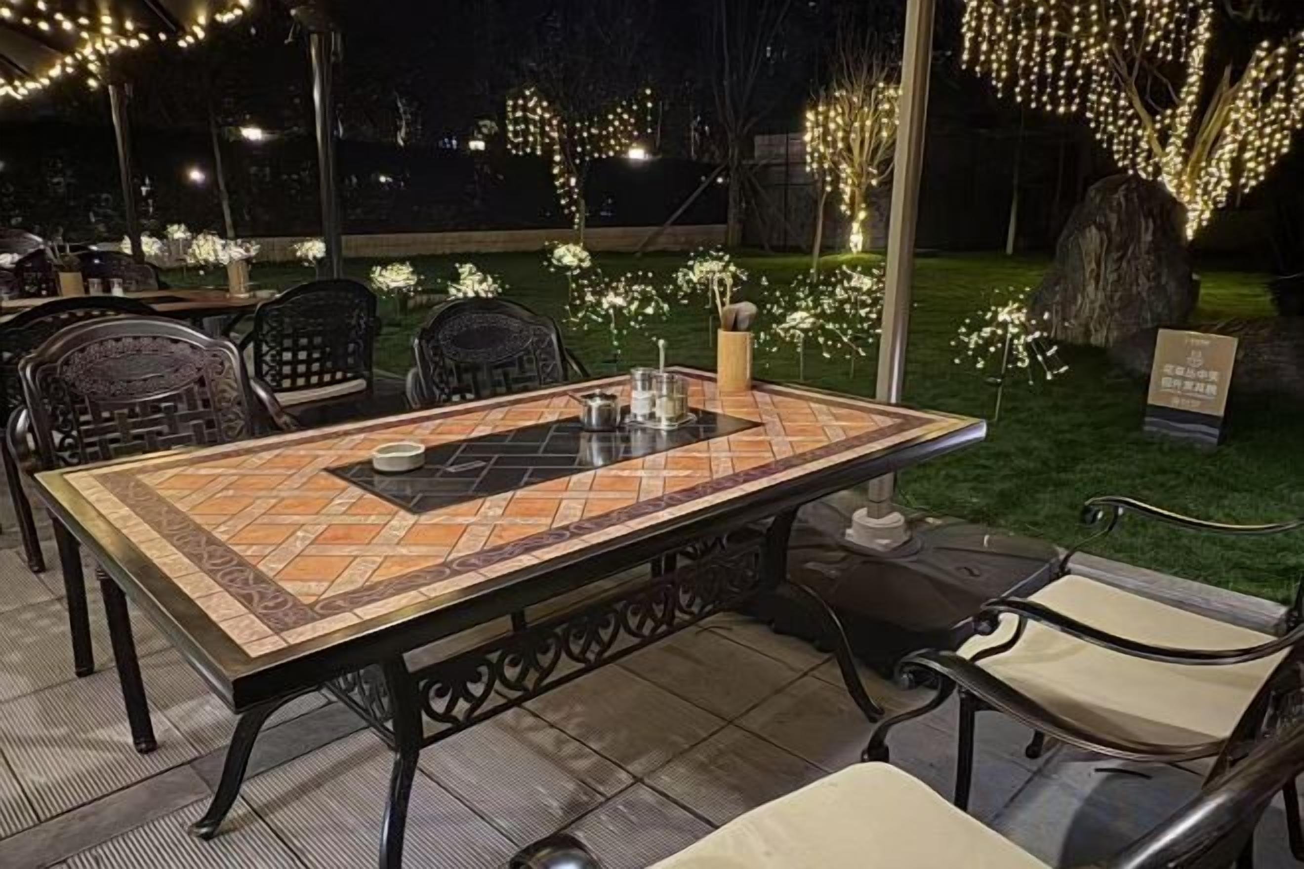 An outdoor dining area with a table and chairs, surrounded by decorative lights and a well-maintained lawn.