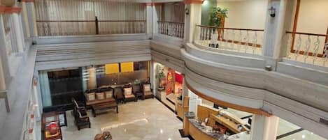 Un hall d’hôtel à plusieurs niveaux, doté d’un espace salon central, d’un comptoir d’accueil et d’un escalier reliant les différents étages.