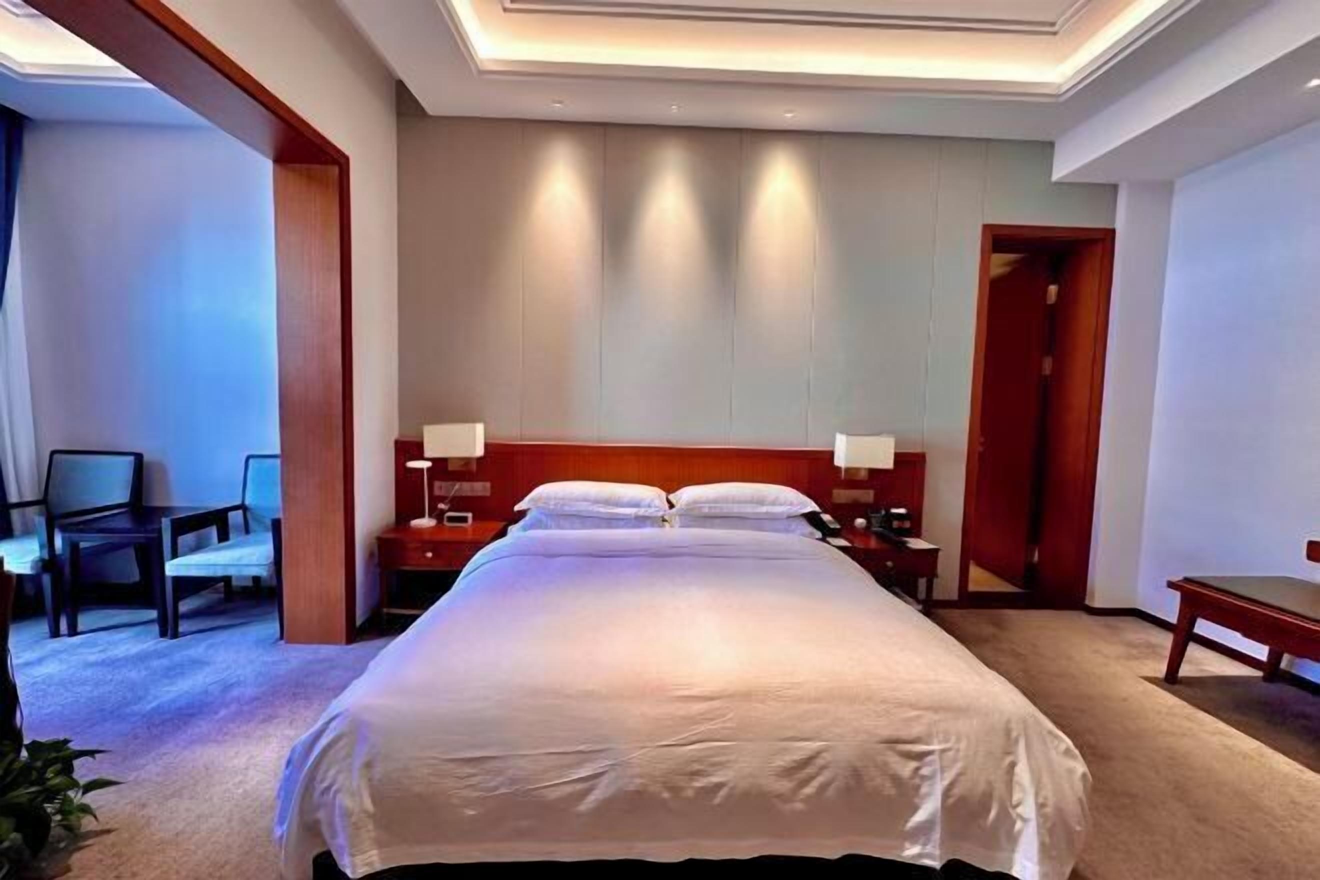A hotel room with a large bed, bedside tables, a desk, and chairs.