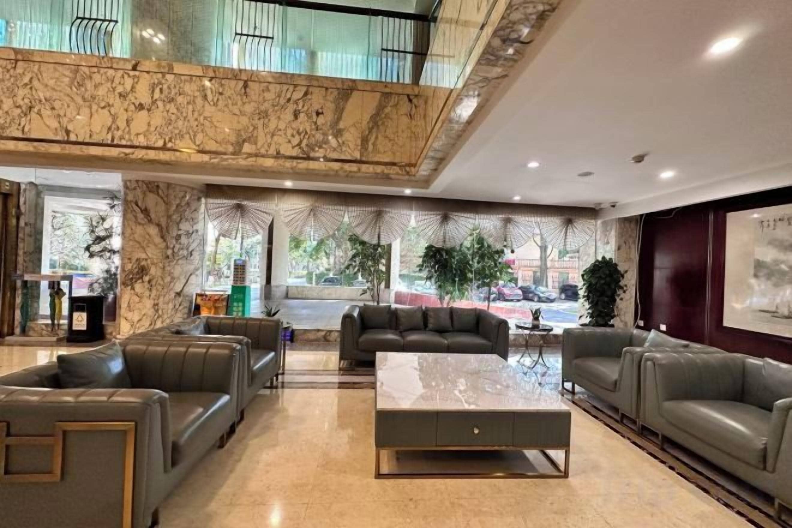 A hotel lobby with marble flooring, leather sofas, a central coffee table, and a view of the street through large windows.