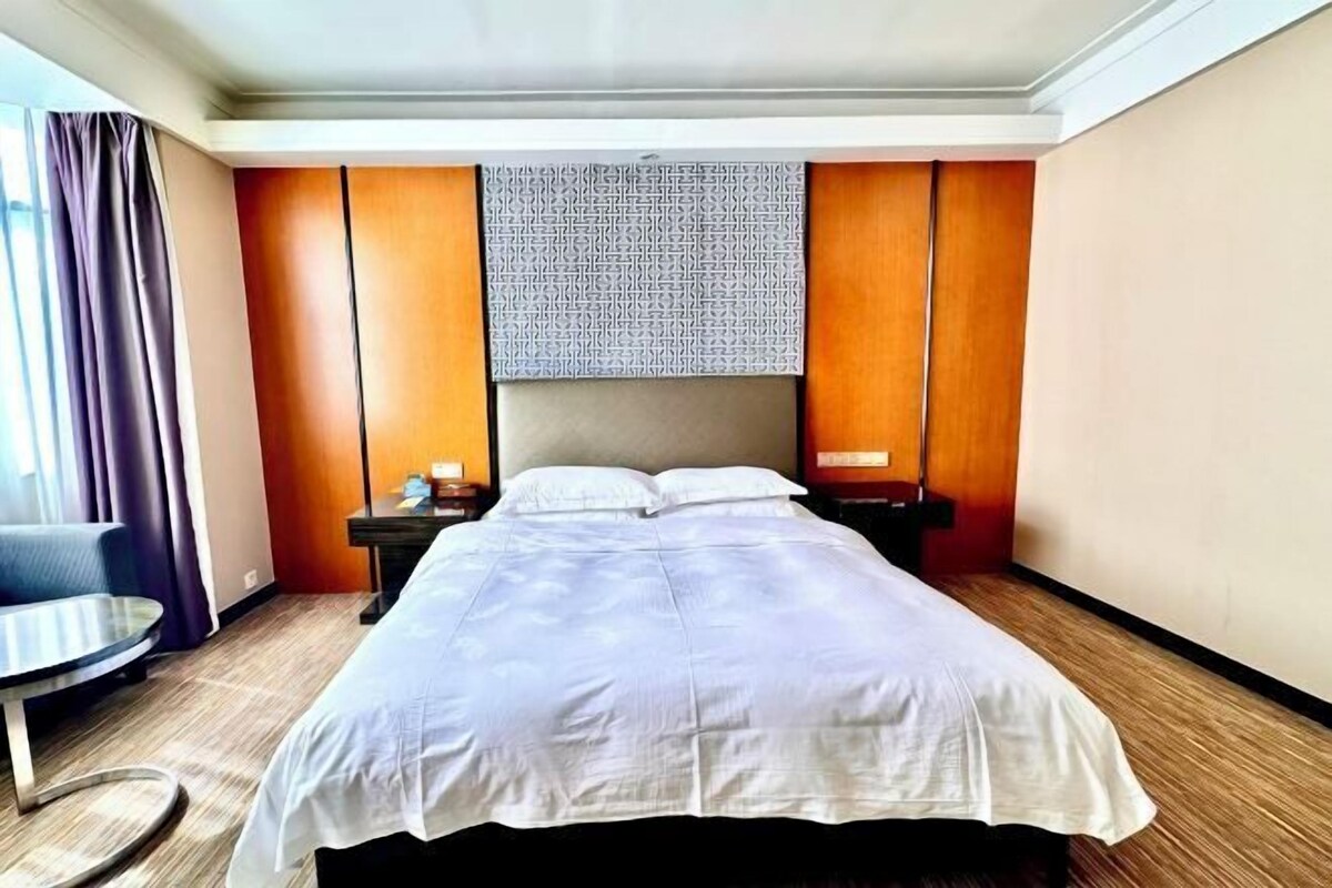 A hotel room with a large bed, a bedside table, a chair, and a view of the outdoors.
