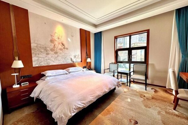A hotel room with a large bed, a desk, two chairs, a window with a view, and a decorative wall mural.
