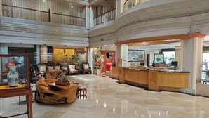 Eine geräumige Lobby mit hoher Decke, einem Empfangstresen und einer Sitzecke mit einem Holztisch.