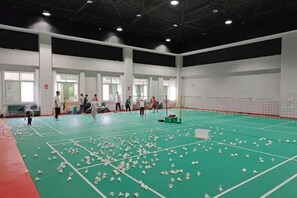 An indoor badminton court with multiple players, a net, and scattered shuttlecocks. - Lian Yun Hotel (Kunming)