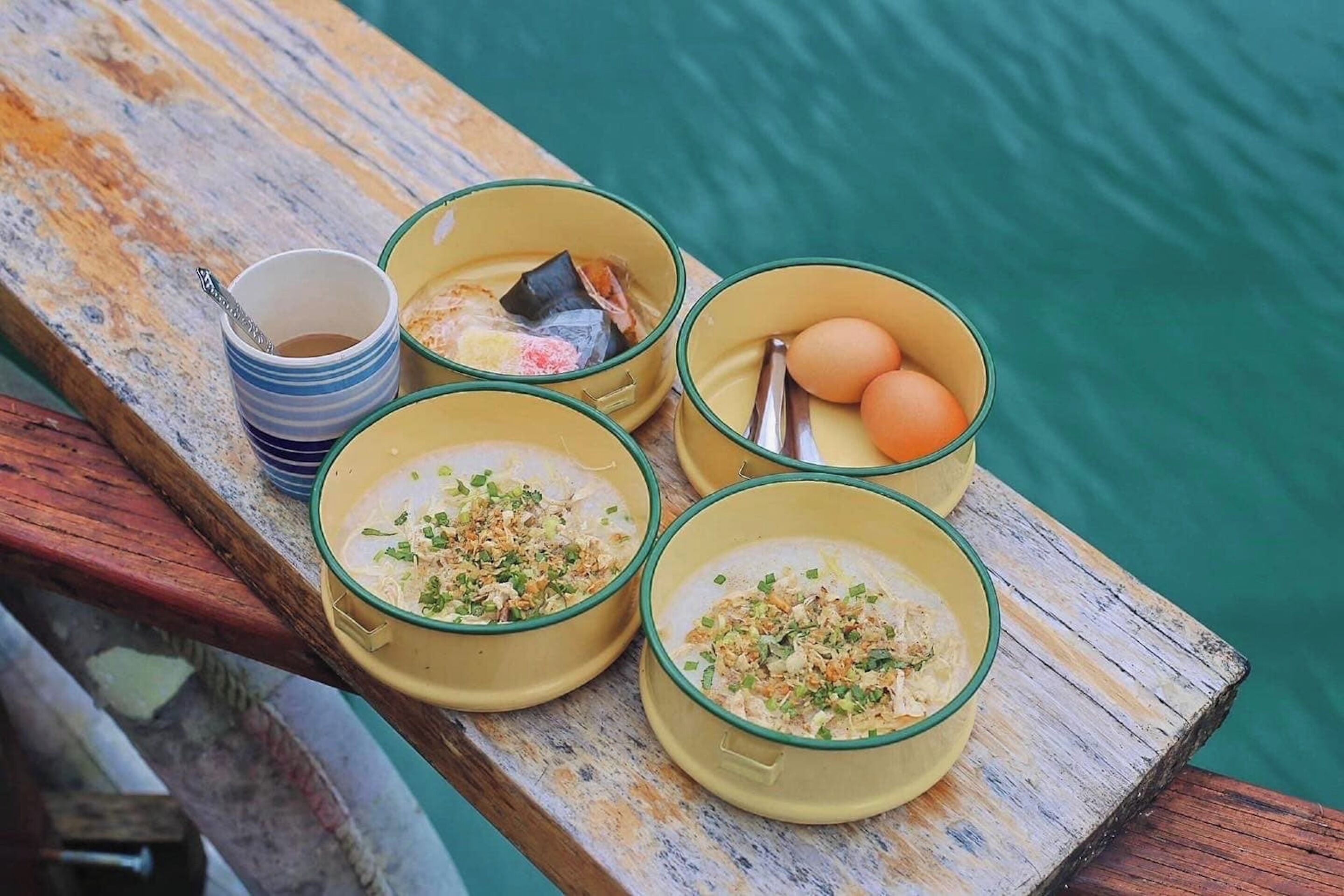 Cuatro platos de comida sobre una mesa de madera cerca del agua.