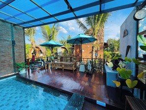An outdoor pool area with wooden deck, lounge chairs, and umbrellas.
