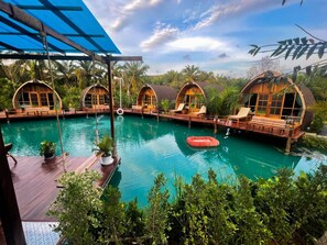 A pool area with wooden cabanas, a wooden deck, and a clear blue pool.