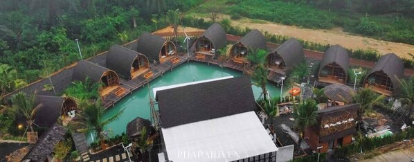 A resort with overwater bungalows, a central pool, and lush greenery.