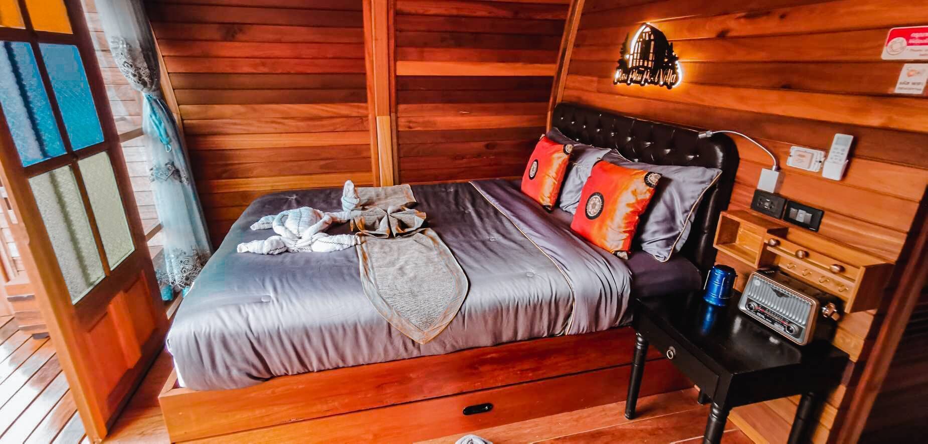 A cozy wooden cabin bedroom with a bed, pillows, a nightstand, and a lamp.