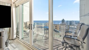 Ein Balkon mit Blick auf das Meer und die Stadt, ausgestattet mit einem Fernseher, Stühlen und einem Tisch.