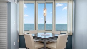 A dining area with a table and chairs, large windows with ocean views, and a hanging light fixture. - Quay - Direct Ocean Front 3 Bedroom Condo with Indoor & Outdoor Pools! (Ocean City)