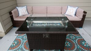 A patio area with a glass-top table, wicker sofa, and patterned rug. - Spacious family retreat with backyard & theater room (Westminster)