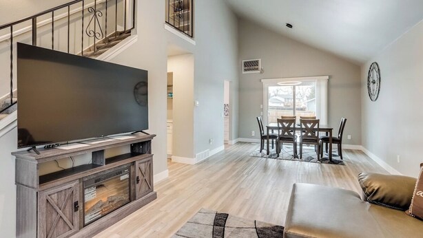 A spacious living room with a large flat-screen TV on a wooden entertainment unit, a dining area with a table and chairs, and a staircase with a railing. - Spacious family retreat with backyard & theater room (Westminster)