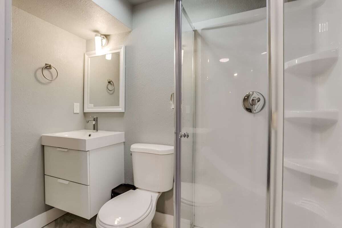 Et moderne badeværelse med en glasbrusekabine, en hvid vask og et toilet.