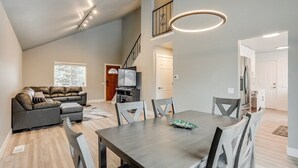 A spacious living area with a dark wood dining table, grey upholstered chairs, a leather sofa, and a flat-screen TV. - Spacious family retreat with backyard & theater room (Westminster)