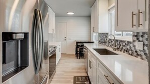 A modern kitchen with white cabinetry, a stainless steel refrigerator, a tiled backsplash, and a wooden floor. - Spacious family retreat with backyard & theater room (Westminster)