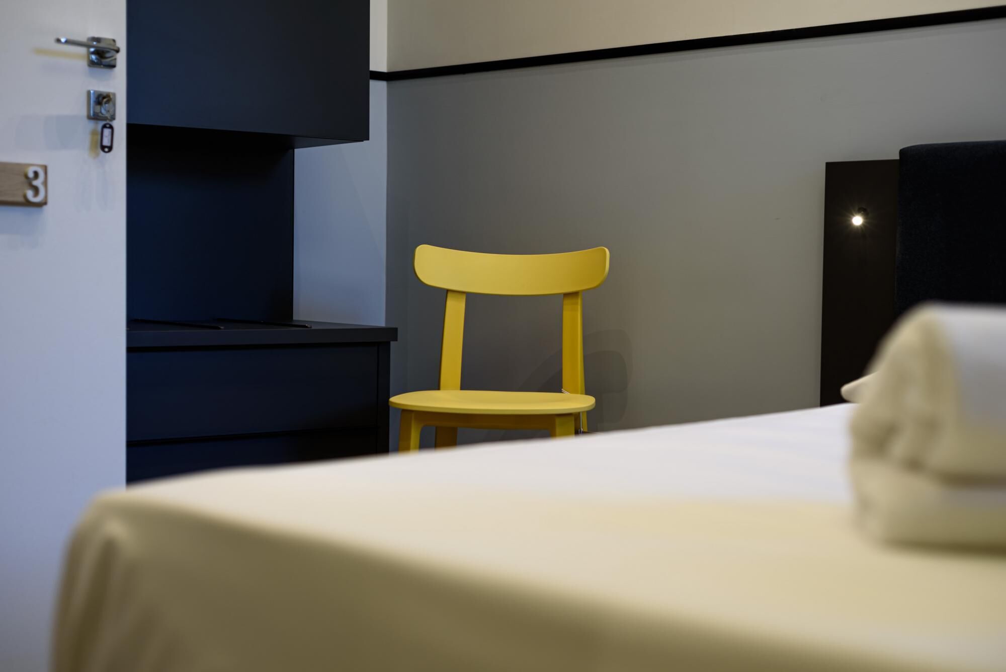 Een hotelkamer met een bed, een gele stoel, een bureau en een kledingkast.