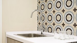 A modern kitchen with a stainless steel sink, white countertop, and patterned tile backsplash. - Maria Theresa Rooms Garden (Naples)