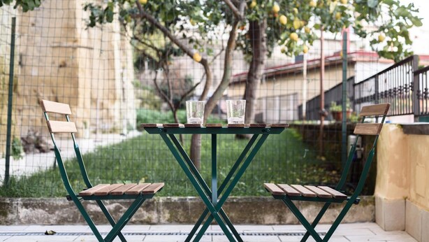 A green metal table with two wooden chairs, each with a wooden seat and backrest. - Maria Theresa Rooms Garden (Naples)