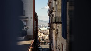 A narrow street with buildings on either side, leading to a distant view of a cityscape with a prominent building labeled "MEDITERRANEO". - Maria Theresa Rooms Garden (Naples)
