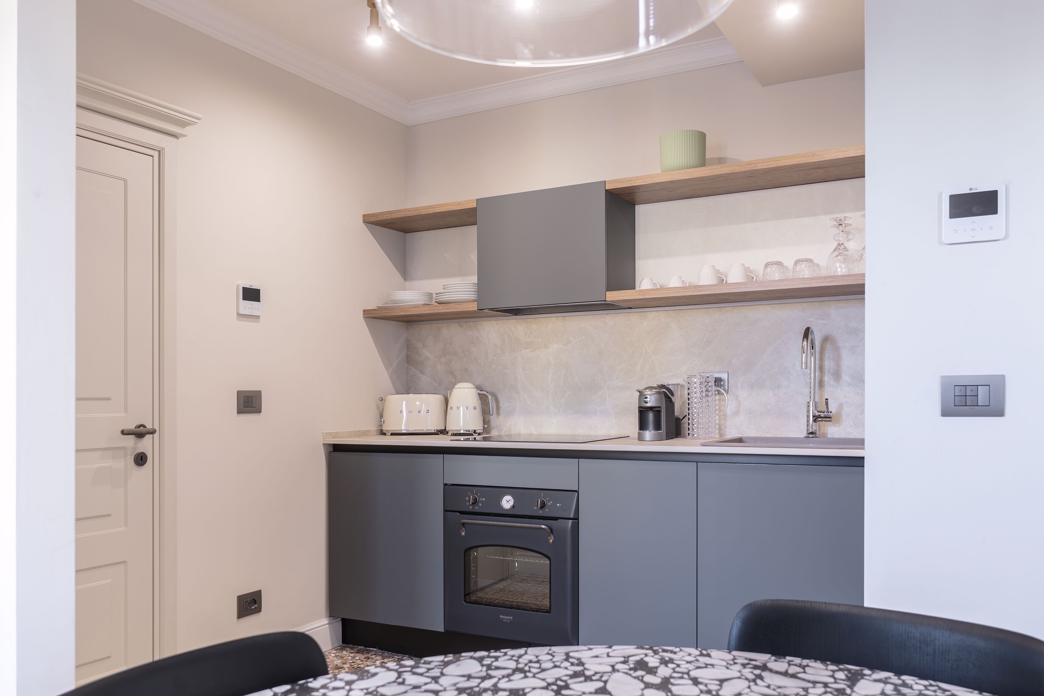 A compact kitchen with built-in appliances, a dining area with a patterned table, and a door with a handle.