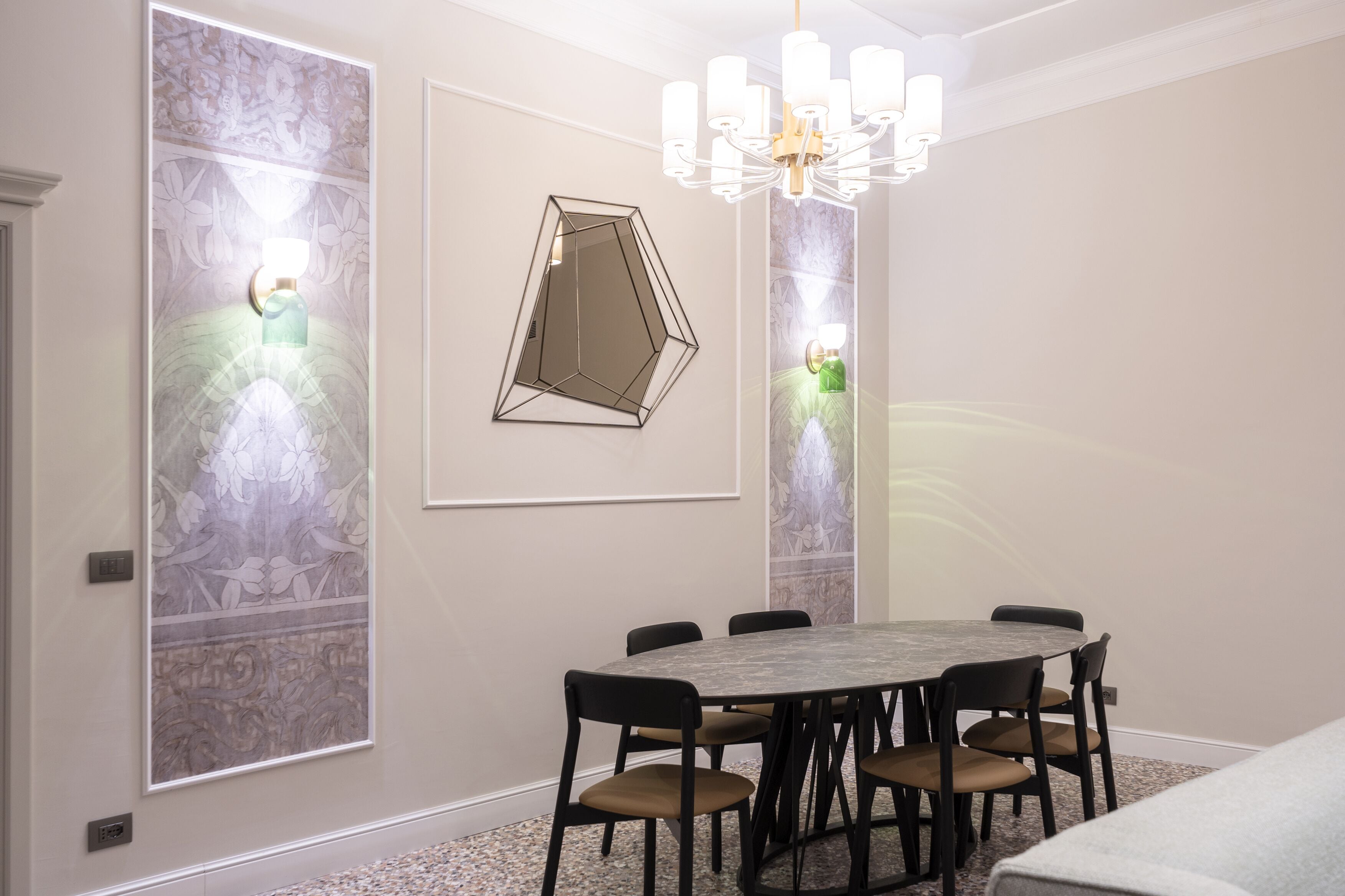 A dining area with a round table, six chairs, a chandelier, and wall-mounted sconces.