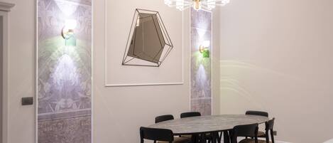 A dining area with a round table, six chairs, a chandelier, and wall-mounted sconces.