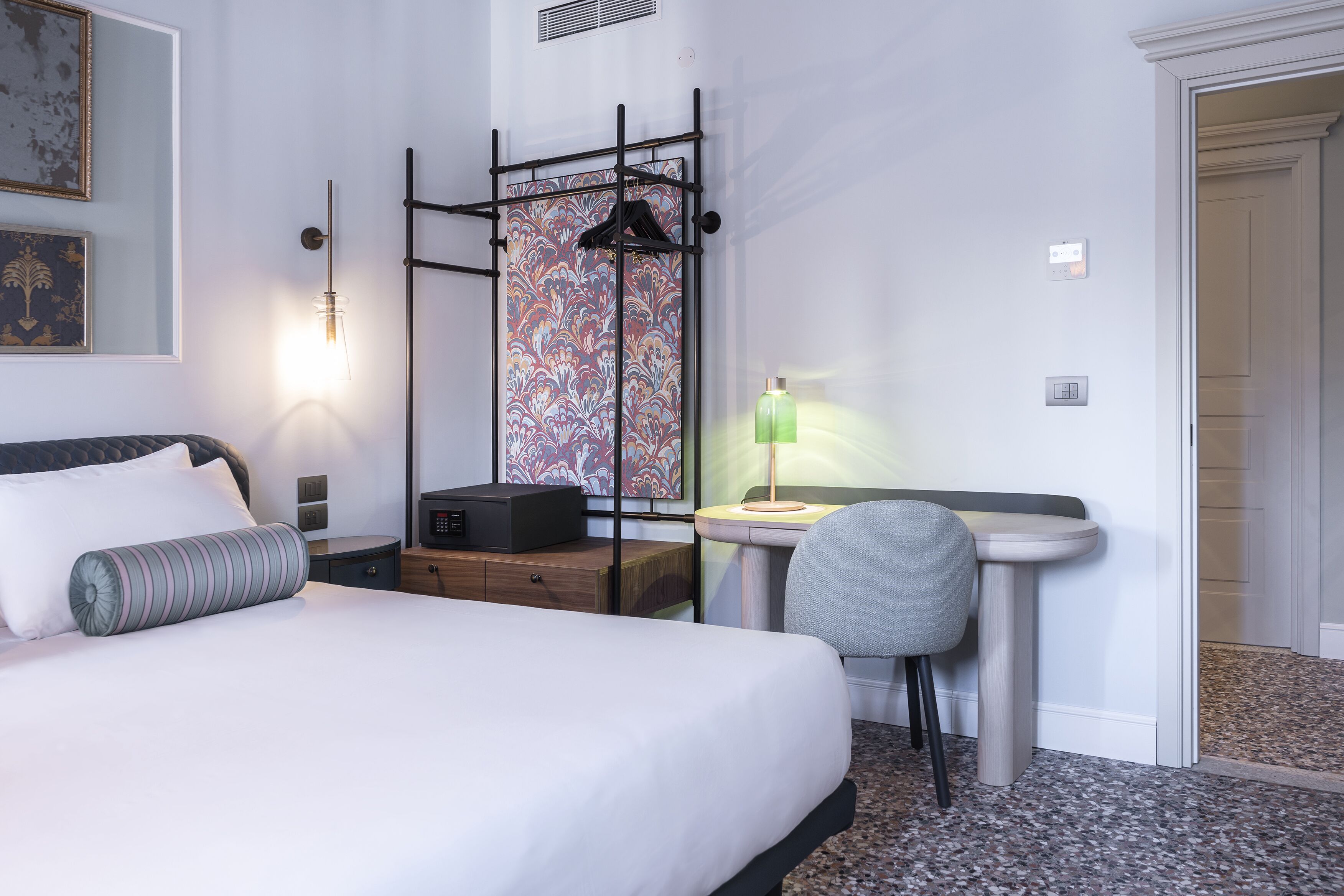 A hotel room with a bed, bedside table, desk, chair, and a small table with a lamp.