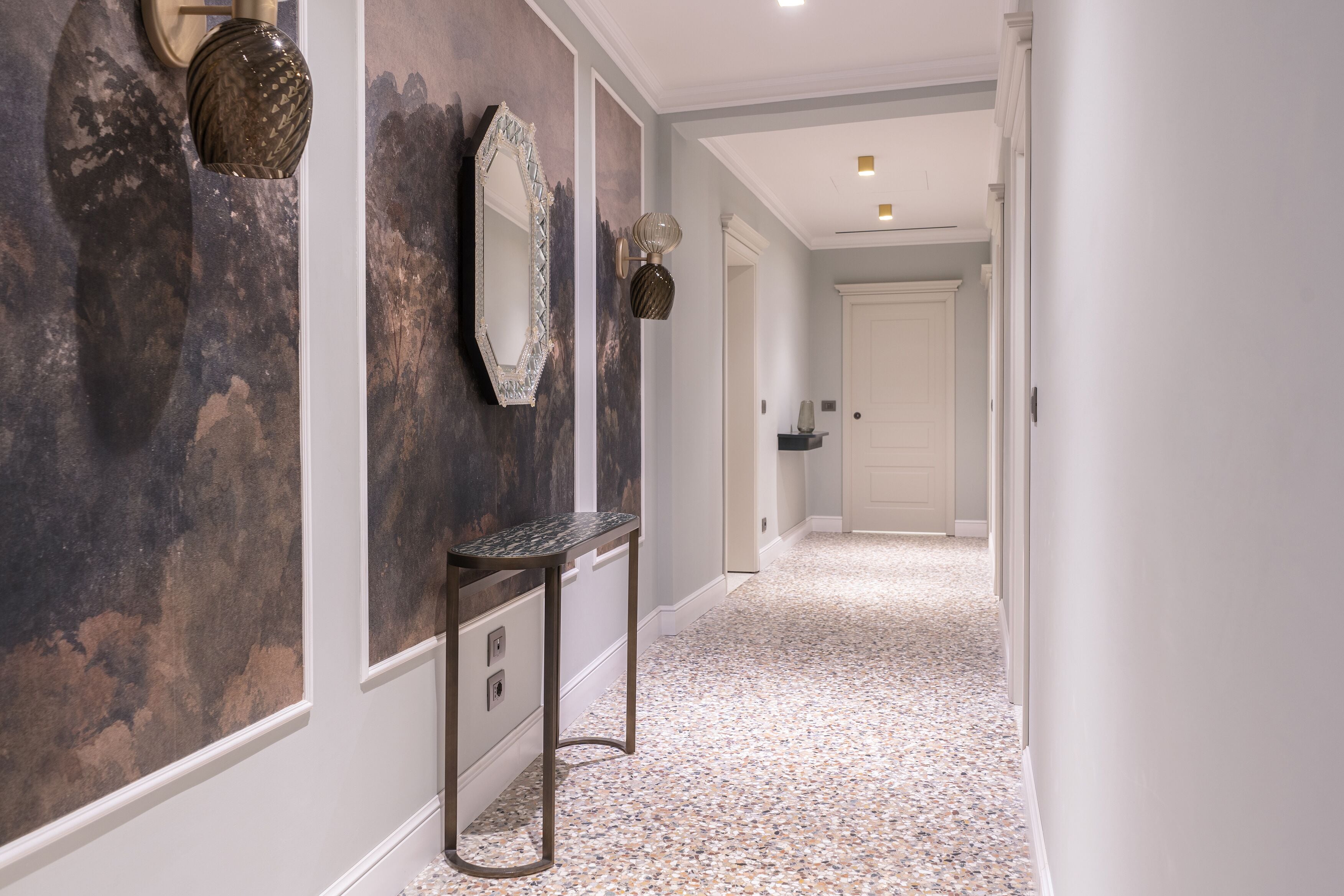 A hallway with a textured wall, a mirror, a console table, and a door at the end.