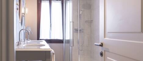 Une salle de bain moderne avec une douche à l’italienne en verre, un meuble-lavabo à deux vasques et une fenêtre avec des rideaux.